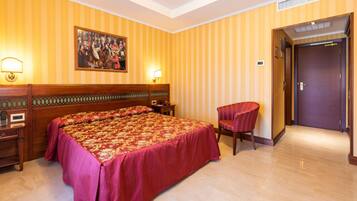 Una habitación de hotel con una cama grande, dos mesitas de noche, una silla y una puerta.