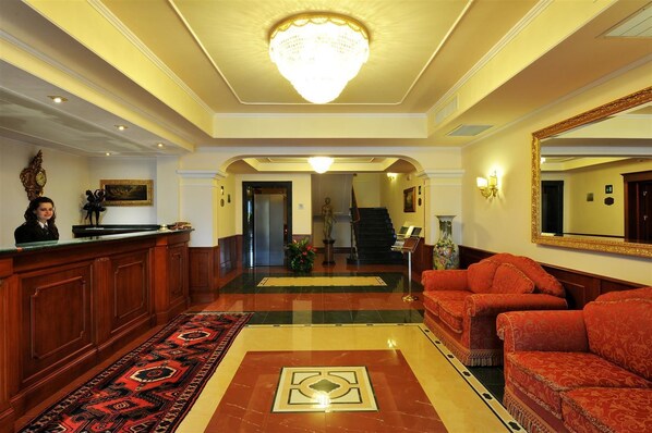 A hotel lobby with a reception desk, a chandelier, a red sofa, and a large mirror.