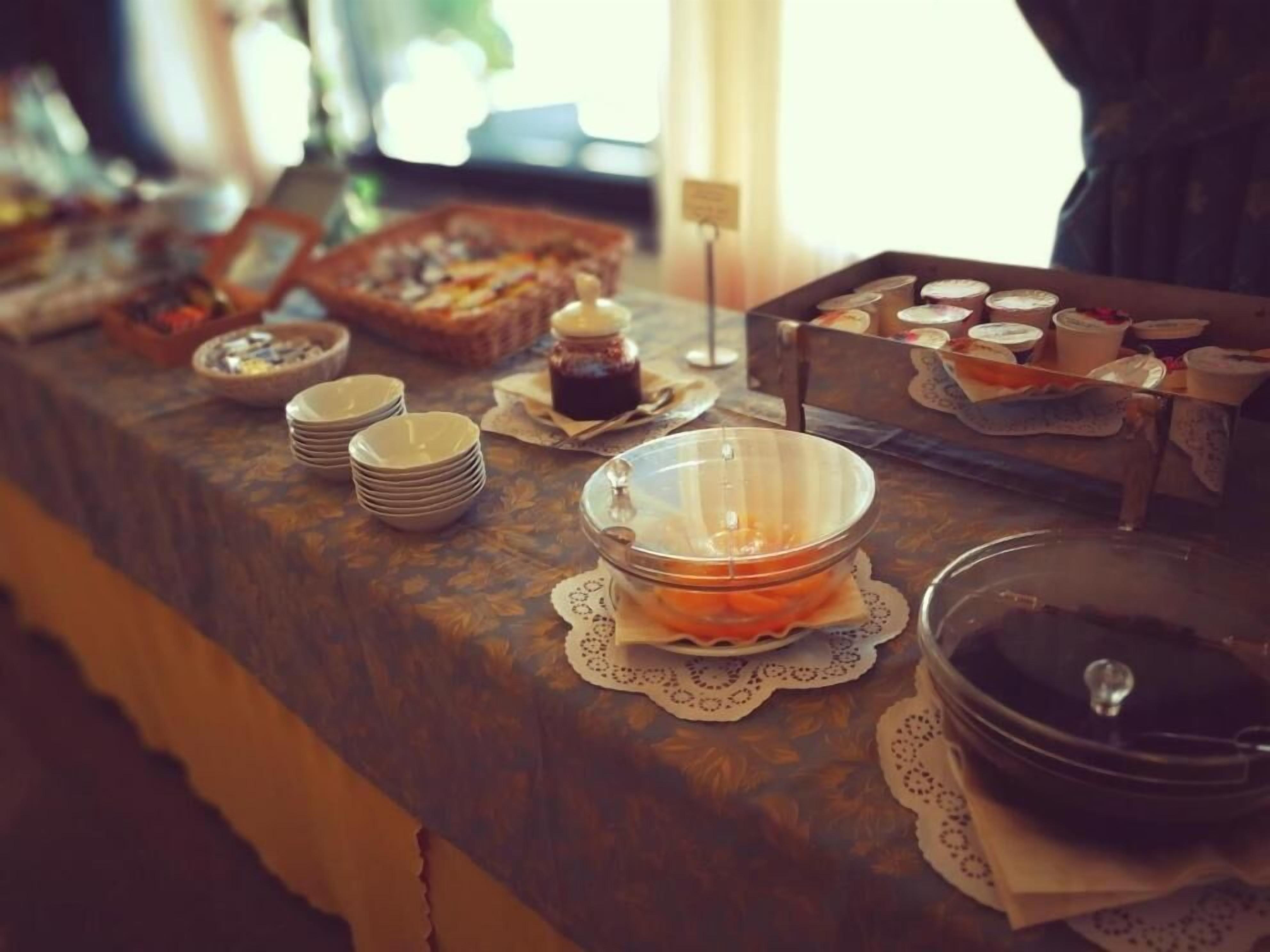 A buffet setup with various dishes and containers, including a bowl of orange slices, a jar of jam, and a tray of cupcakes.