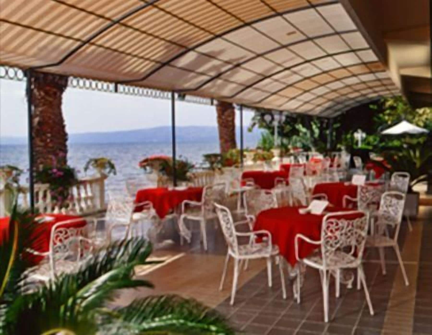 Un área de comedor al aire libre con mesas y sillas, techo cubierto y vista al mar.