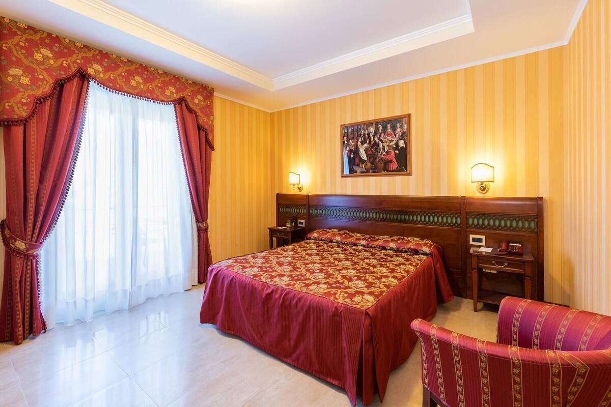 A hotel room with a large bed, two bedside tables, a chair, and a painting on the wall.