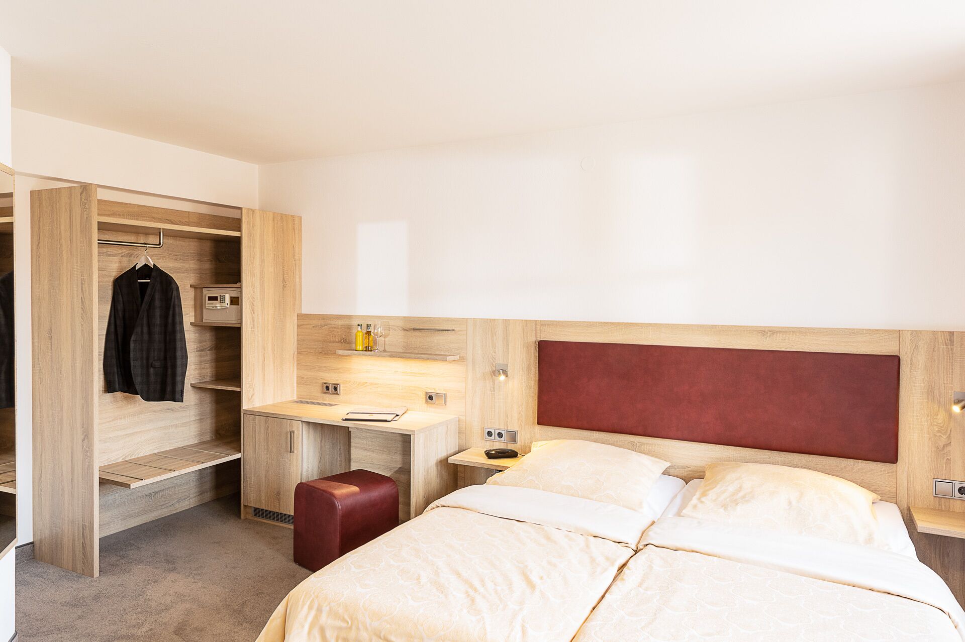 Una habitación de hotel con cama, escritorio, armario y un otoman rojo.