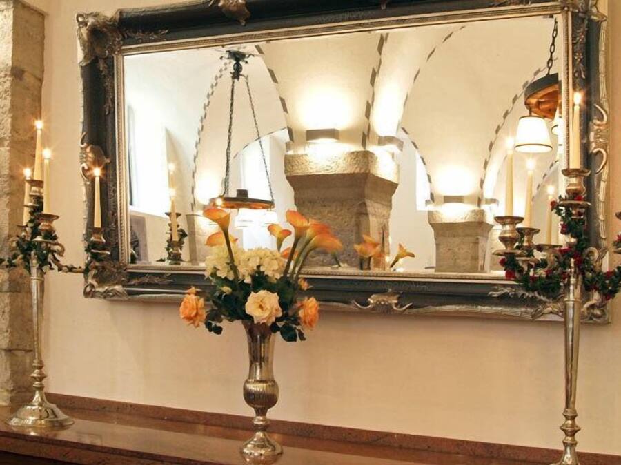 Un espejo con un marco decorativo, un jarrón con flores y candelabros en una pared.
