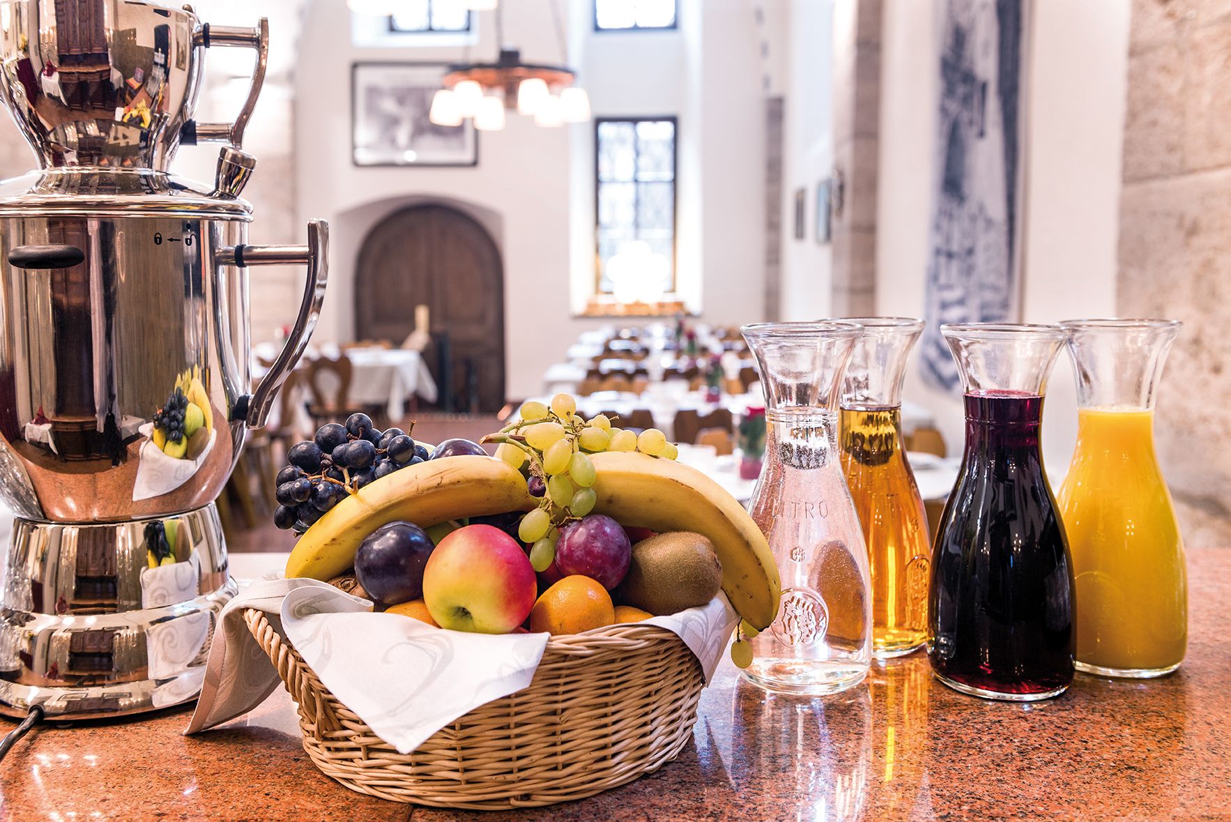 A breakfast buffet with fruits, a coffee pot, and juice bottles on a counter.
