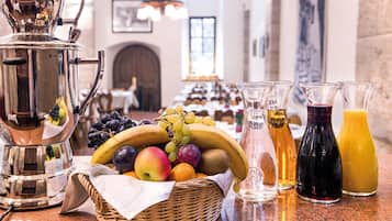 A breakfast buffet with fruits, a coffee pot, and juice bottles on a counter.