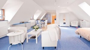 A modern, well-lit room with a high ceiling and skylights, featuring a white sofa, a small round table, and a white armchair. - Hotel Garni Altes Brauhaus (Rothenburg ob der Tauber)
