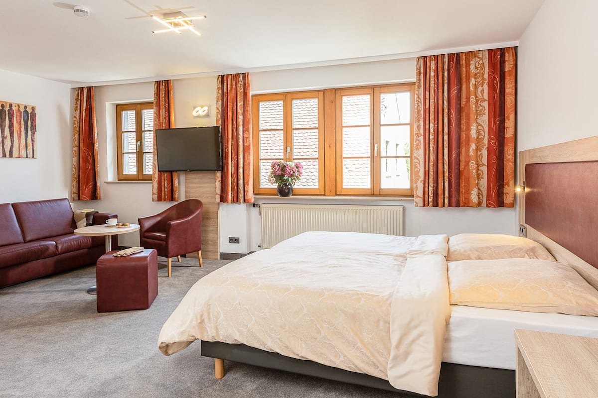 Habitación de hotel con cama, sofá, sillón, mesita y televisión.