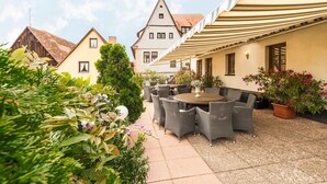 An outdoor patio with wicker furniture and potted plants, surrounded by buildings with traditional architecture. - Hotel Garni Altes Brauhaus (Rothenburg ob der Tauber)