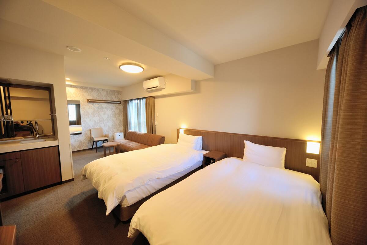 A hotel room with two beds, a bathroom, and a sitting area with a chair and table.