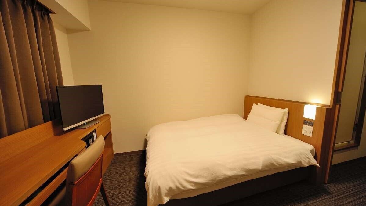 Ein Hotelzimmer mit einem Bett, einem Fernseher auf einer Holzkommode und einem Spiegel an der Wand.