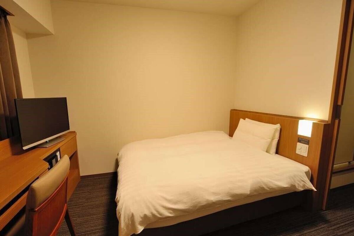 A hotel room with a bed, a television on a wooden dresser, and a mirror on the wall.