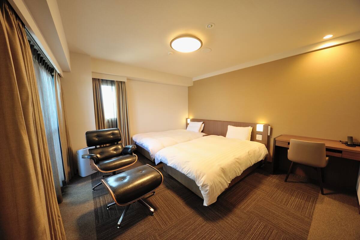 A hotel room with a double bed, a desk, a chair, and a seating area with a sofa and armchair.