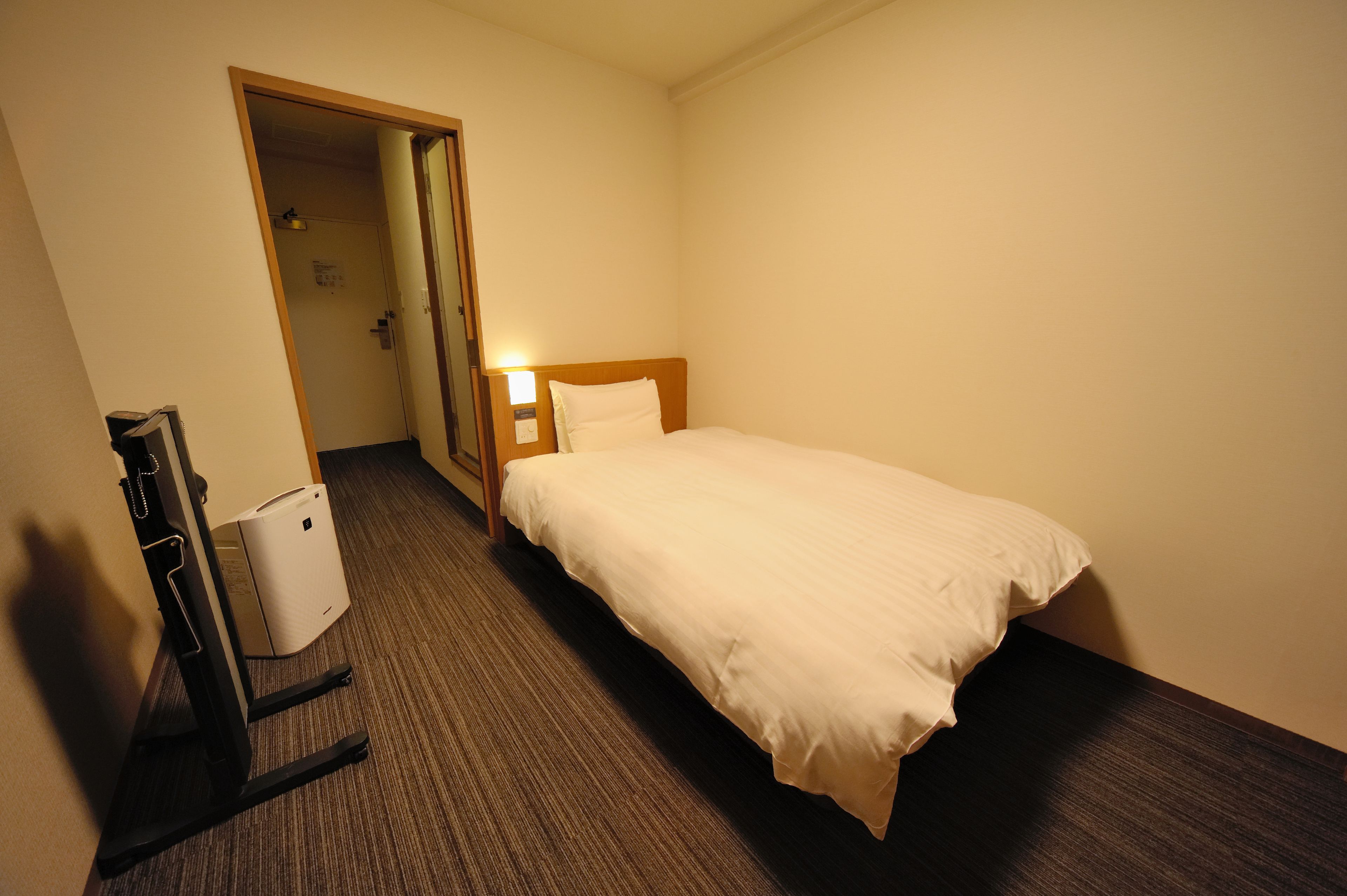 Een hotelkamer met een bed, een bureau, een stoel en een prullenbak.