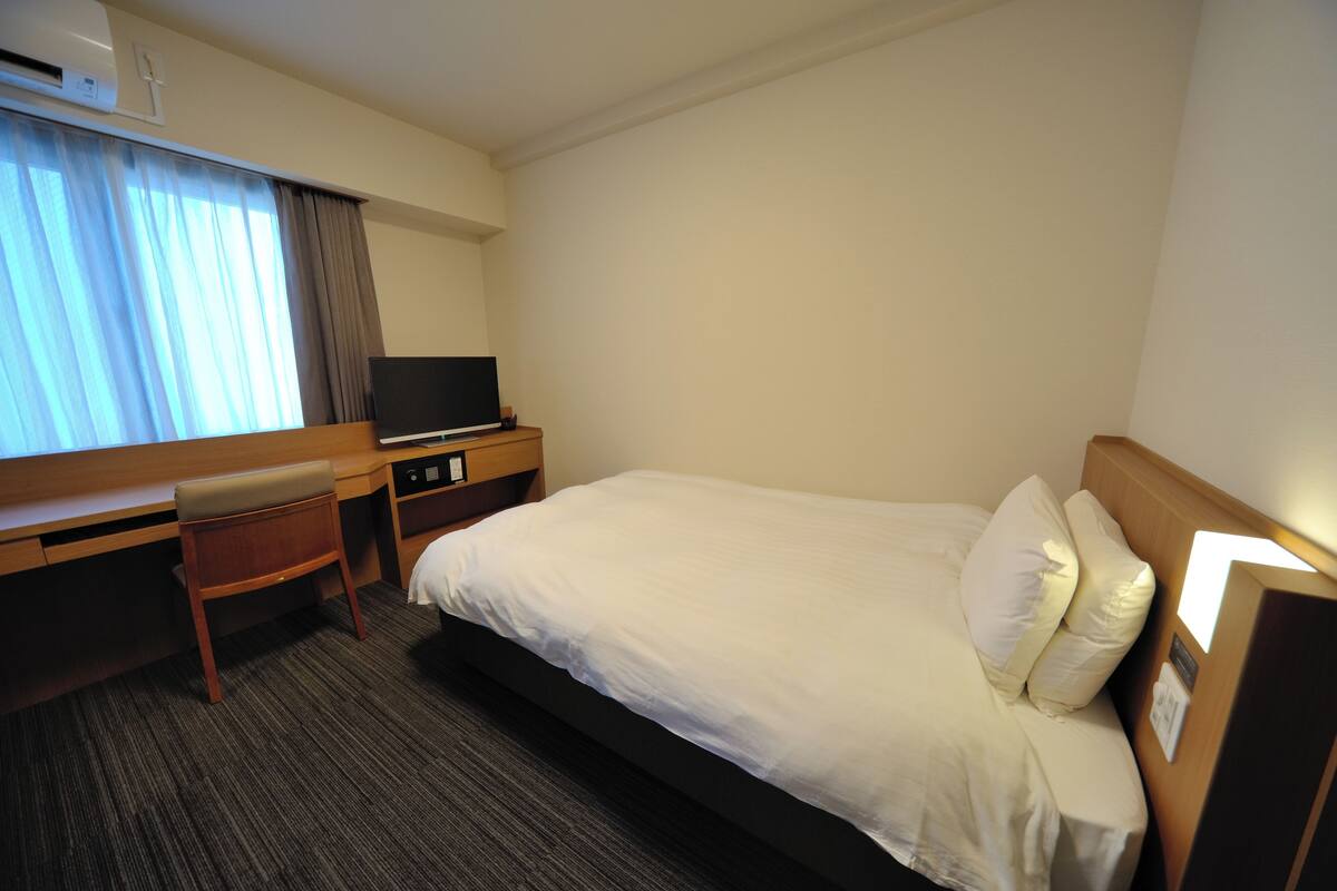 A hotel room with a bed, a desk, a chair, a television, and a window with curtains.