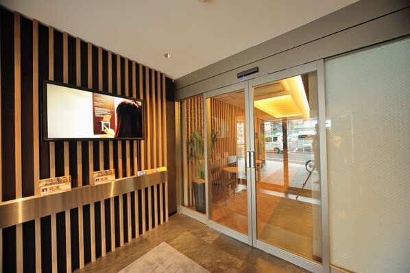 A reception area with a modern design, featuring a reception desk, a digital display, and a glass door leading to the lobby. - Dormy Inn EXPRESS Meguro Aobadai Hot Spring (Tokyo)