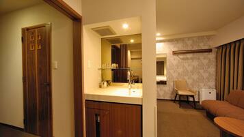 Una habitación de hotel con una puerta de madera, una kitchenette con un lavabo, una silla y un sofá.