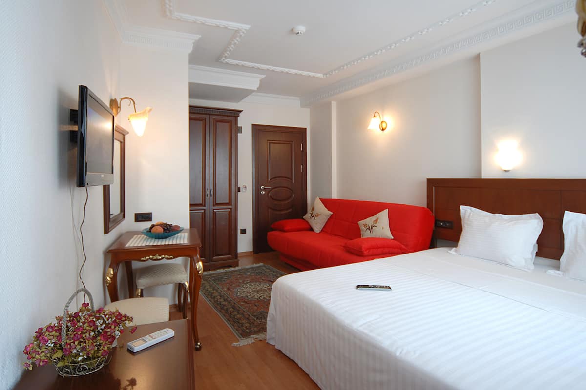 A hotel room with a bed, a desk with a chair, a television, and a red sofa.