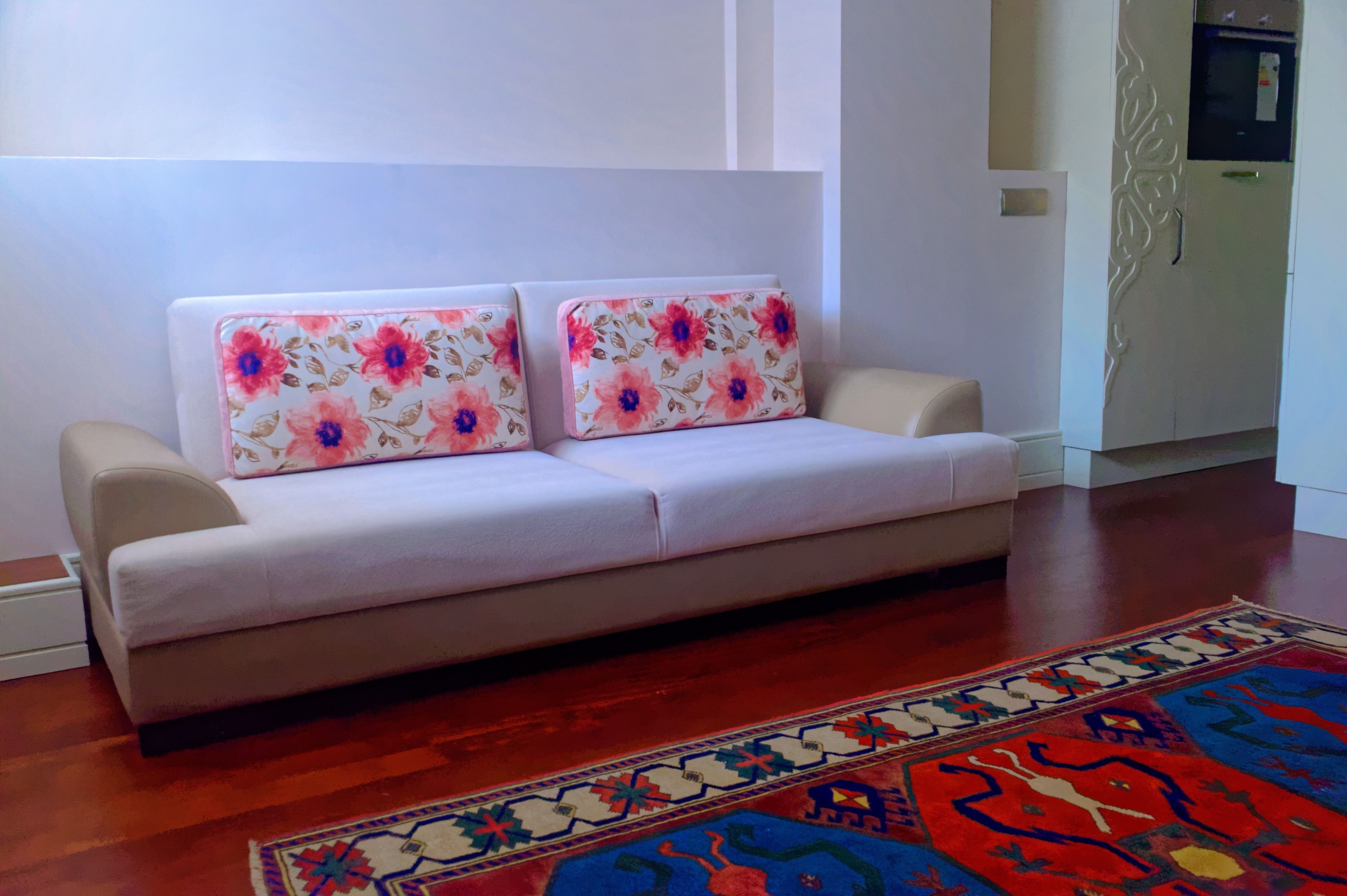 A sofa with floral cushions, a patterned rug, and a kitchen area in the background.