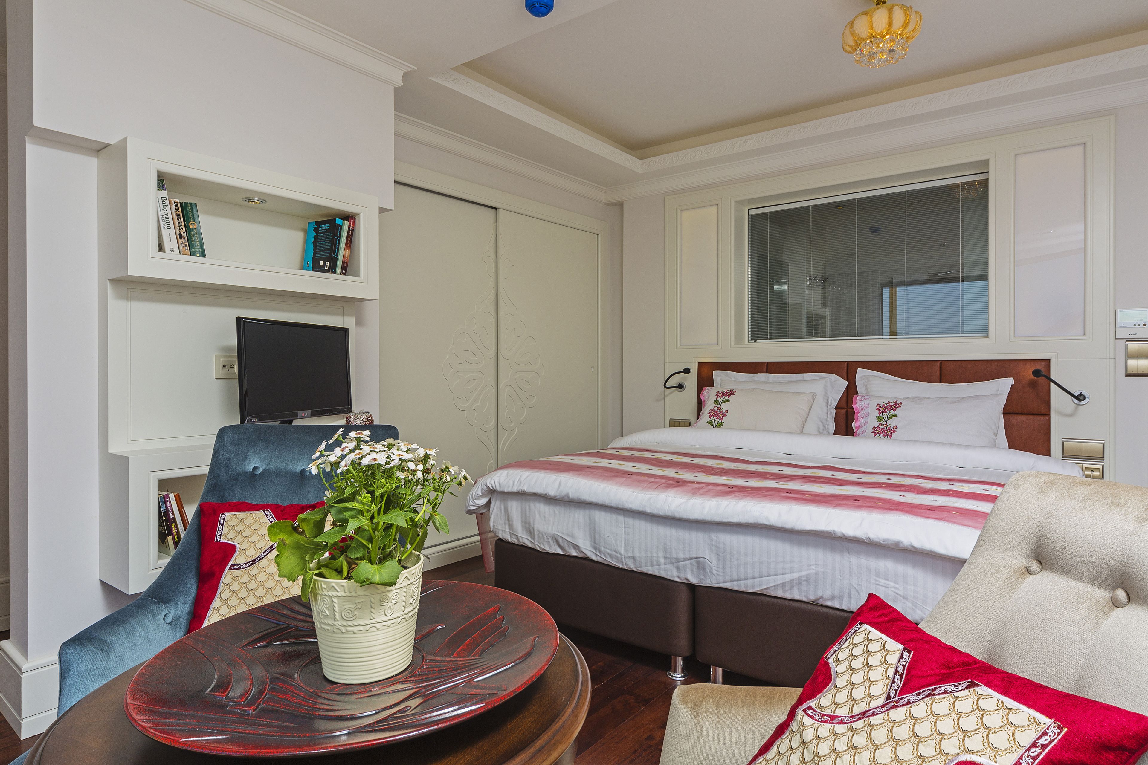 Un dormitorio ordenado con cama, televisor, estantería y zona de comedor con mesa y sillas.