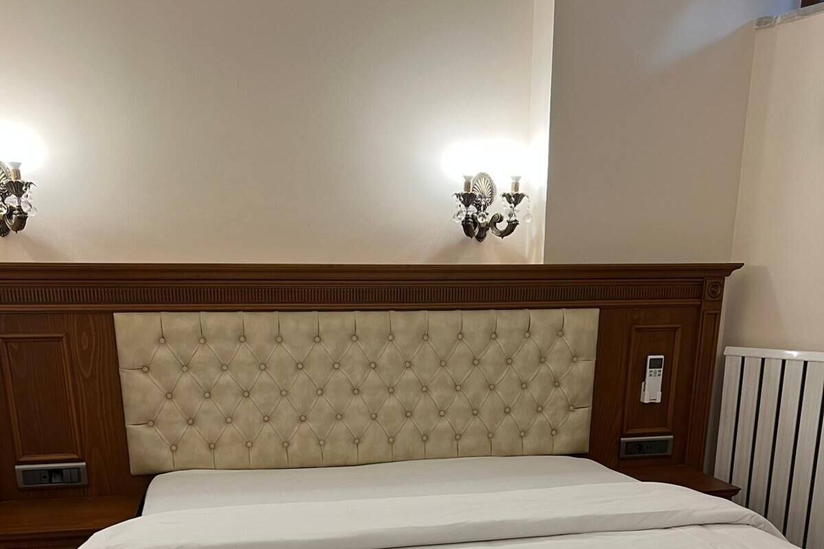 A double bed with a tufted headboard, bedside tables, and wall sconces.