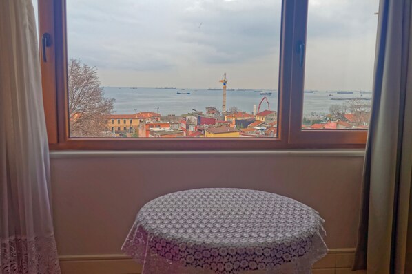 A room with a view of a harbor, a table with a lace tablecloth, and a window with curtains.