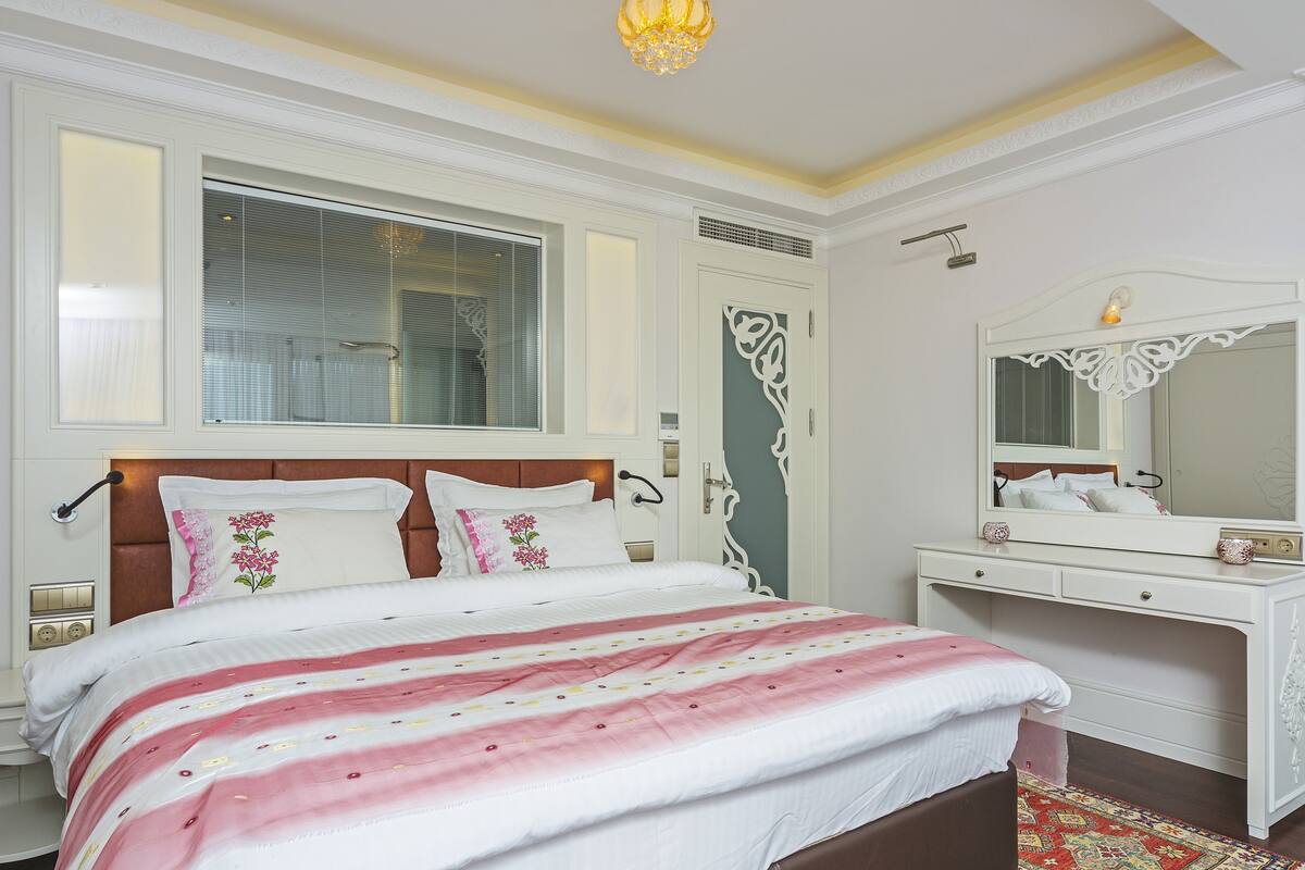 A bedroom with a bed, bedside table, dresser, and a large mirror.