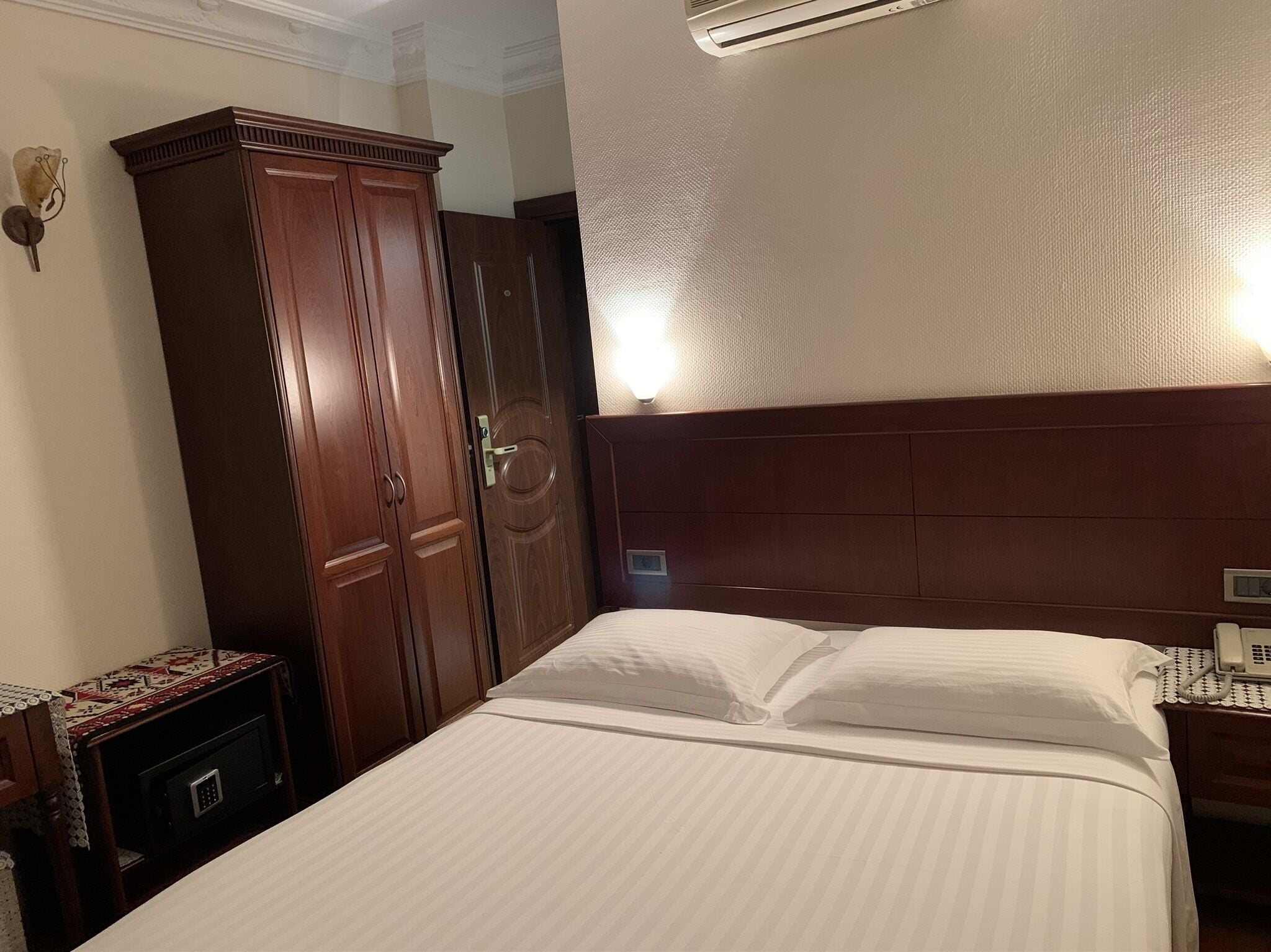 A hotel room with a large bed, a wooden wardrobe, a bedside table, and a nightstand with a telephone.