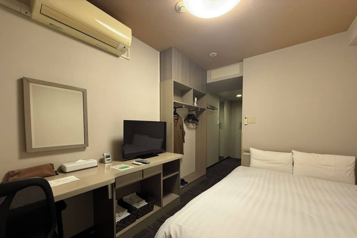 A hotel room with a bed, a desk with a computer, a television, and a wardrobe.
