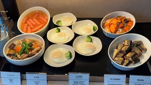 A buffet with various dishes including fried eggs, carrots, broccoli, and fish.