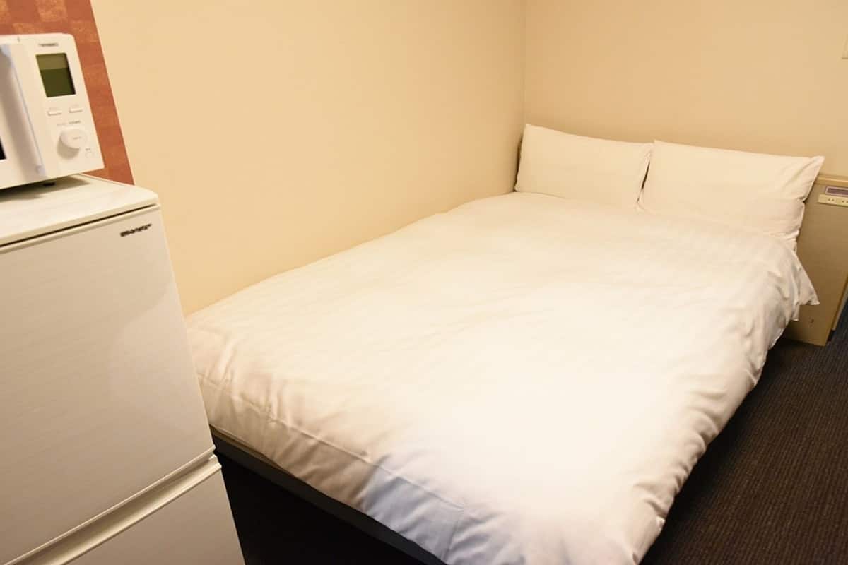 A hotel room with a bed, a white refrigerator, and a microwave on top of it.