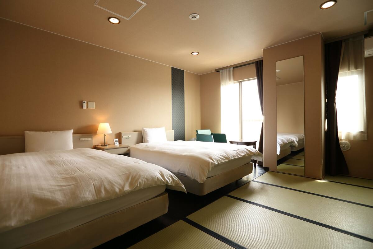 A hotel room with two beds, a sitting area, a large mirror, and a view of the outside.