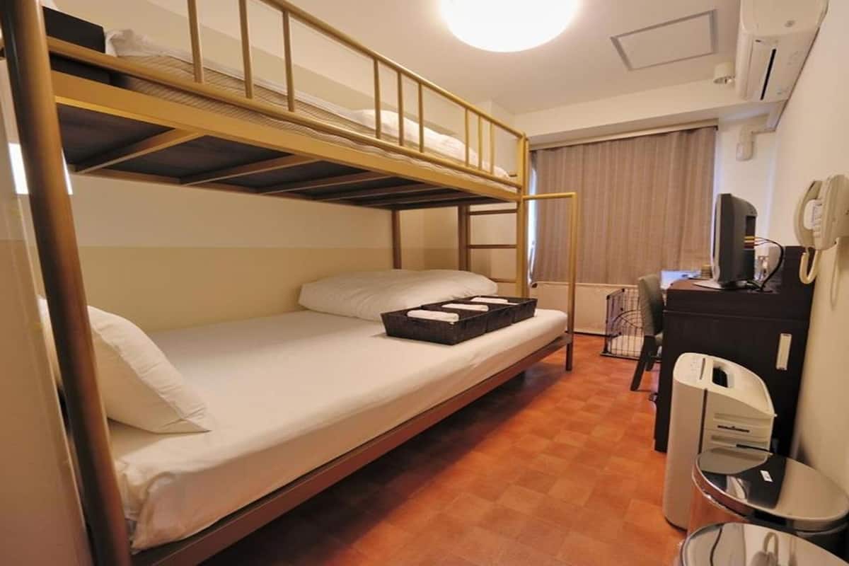 A compact hotel room with a bunk bed, a desk, a chair, and a small trash bin.