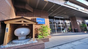 A building entrance with a large stone sculpture, a sign for 'Express Dormy Inn', and a modern glass door.