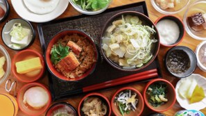A variety of dishes on a wooden table, including bowls of rice, soup, and other foods, with chopsticks and small dishes.