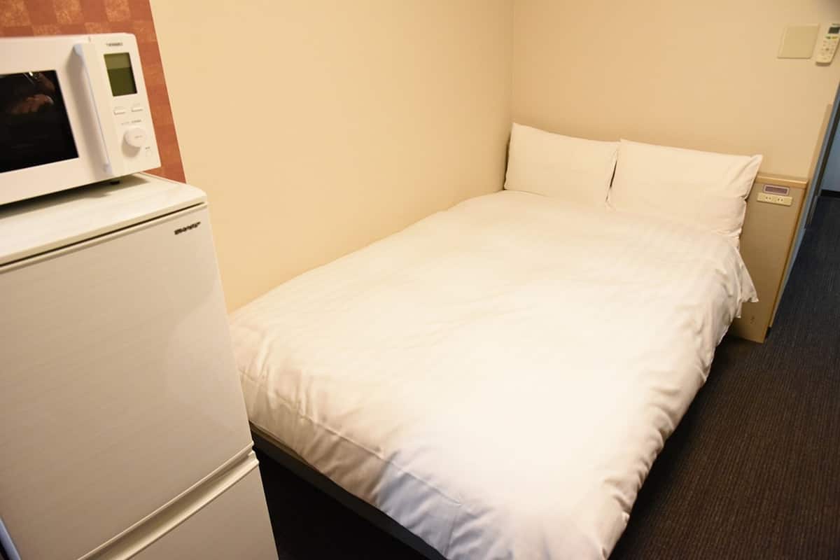 A hotel room with a bed, a white bedside table, and a microwave.