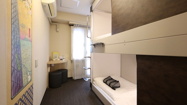A compact hotel room with bunk beds, a small desk with a chair, a trash bin, and a window with curtains. - Dormy Inn Express Asakusa Hot Spring (Tokyo)