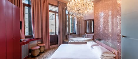 A spacious bedroom with a large bed, a sitting area with a bathtub, and a view of the city through large windows.