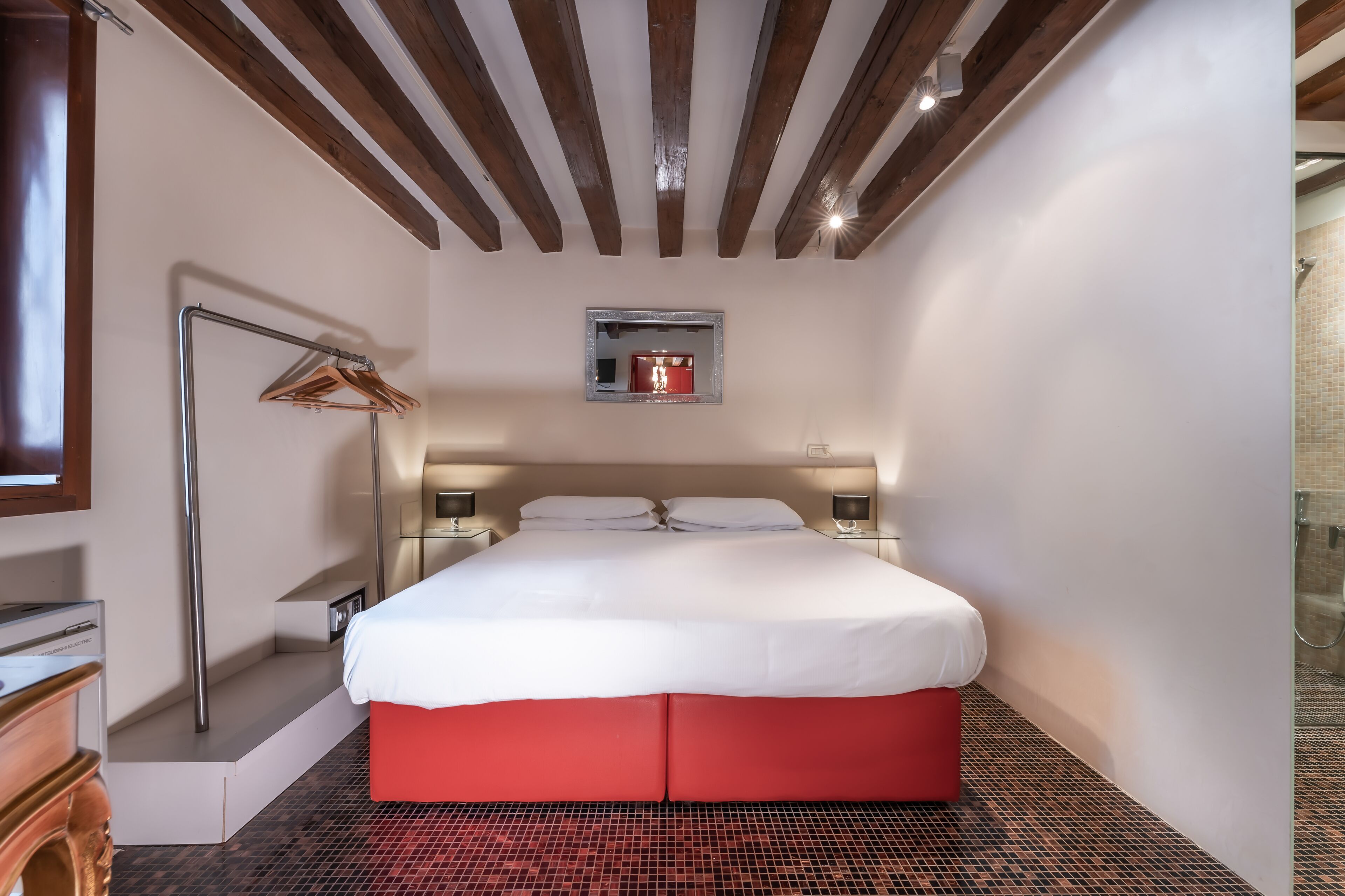 Une chambre d’hôtel avec un lit, des tables de chevet, un miroir et un mur d’accent de couleur rouge.