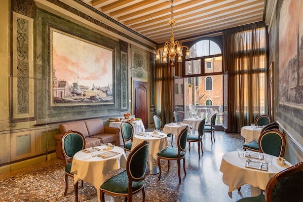 Classic European dining area with round tables, ornate painting, and chandelier.