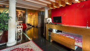 A lobby with a red reception desk, a wooden bench, a white chair, and a large column. - Il sogno di Giulietta e Romeo (Venice)