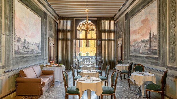 A dining area with round tables, green upholstered chairs, and a view of a building through a large window. - Il sogno di Giulietta e Romeo (Venice)