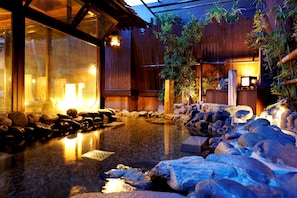 A traditional Japanese onsen with a wooden interior, a stone hot spring surrounded by rocks, and a wooden fence enclosing the area. - Dormy Inn Akihabara Hot Spring (Tokyo)