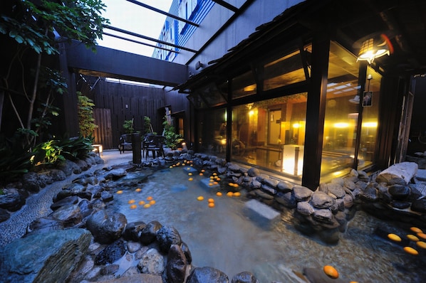 A serene indoor garden with a koi pond, stone pathway, and wooden seating area.