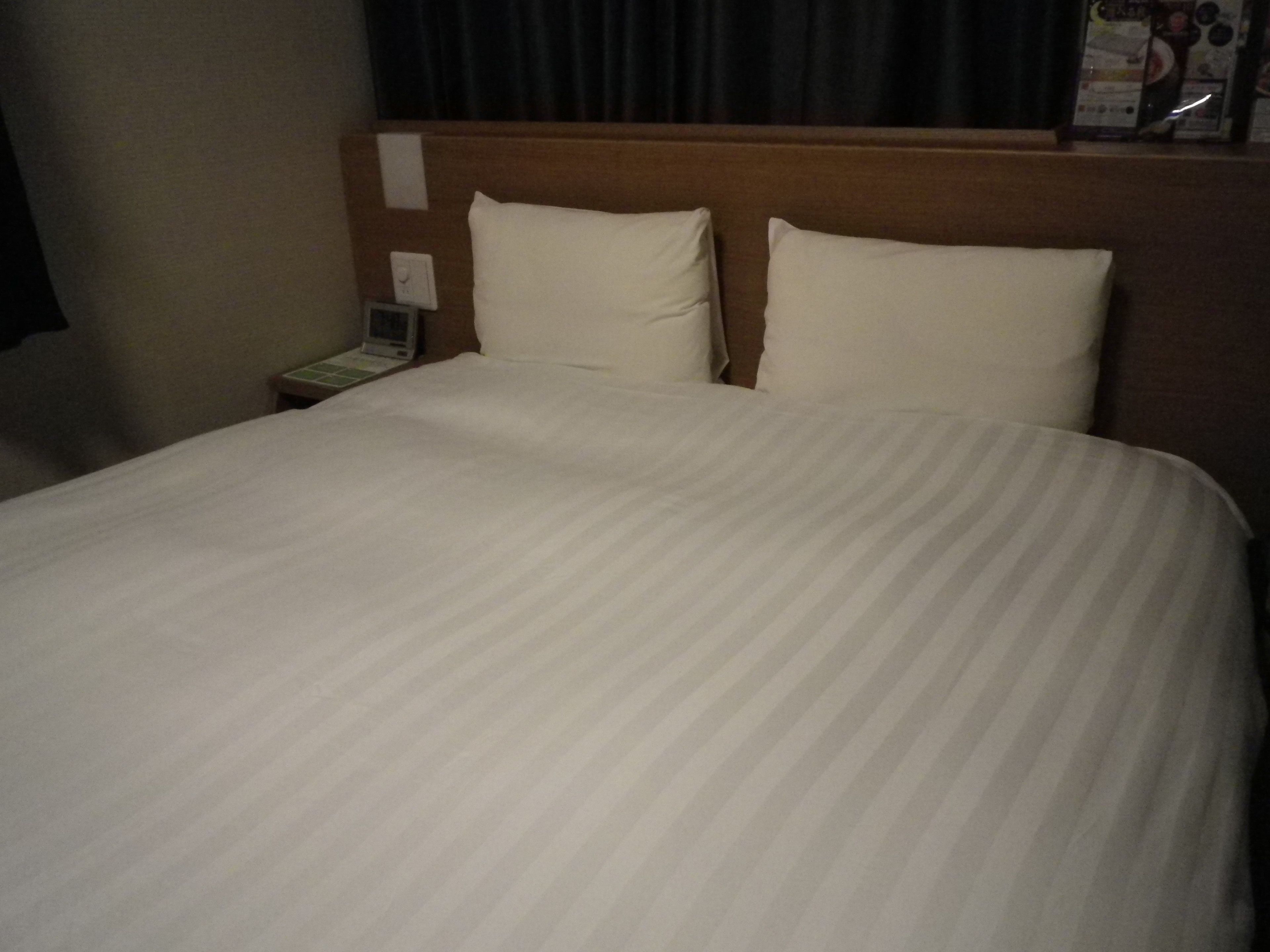 A neatly made bed with a striped bedspread, a wooden headboard, and a nightstand with a telephone and a lamp.