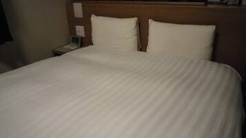A neatly made bed with a striped bedspread, a wooden headboard, and a nightstand with a telephone and a lamp.