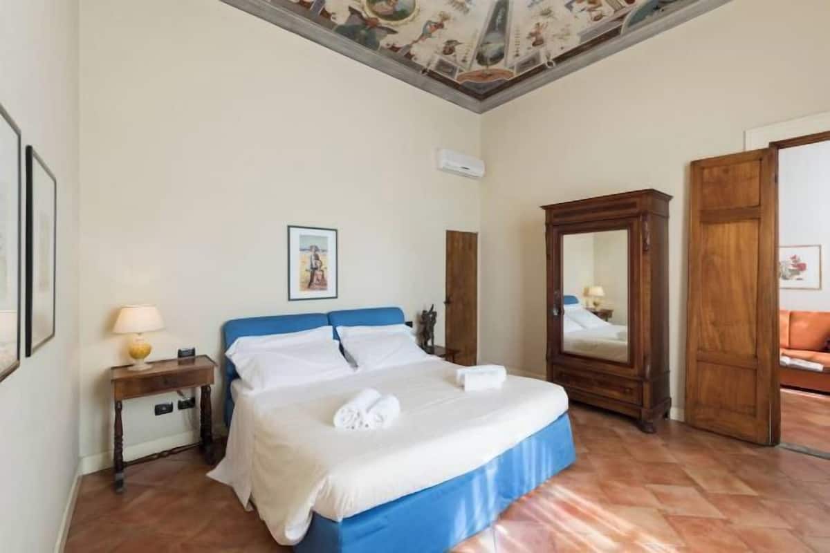 A hotel room with a bed, a nightstand, a mirror, and a wooden wardrobe.