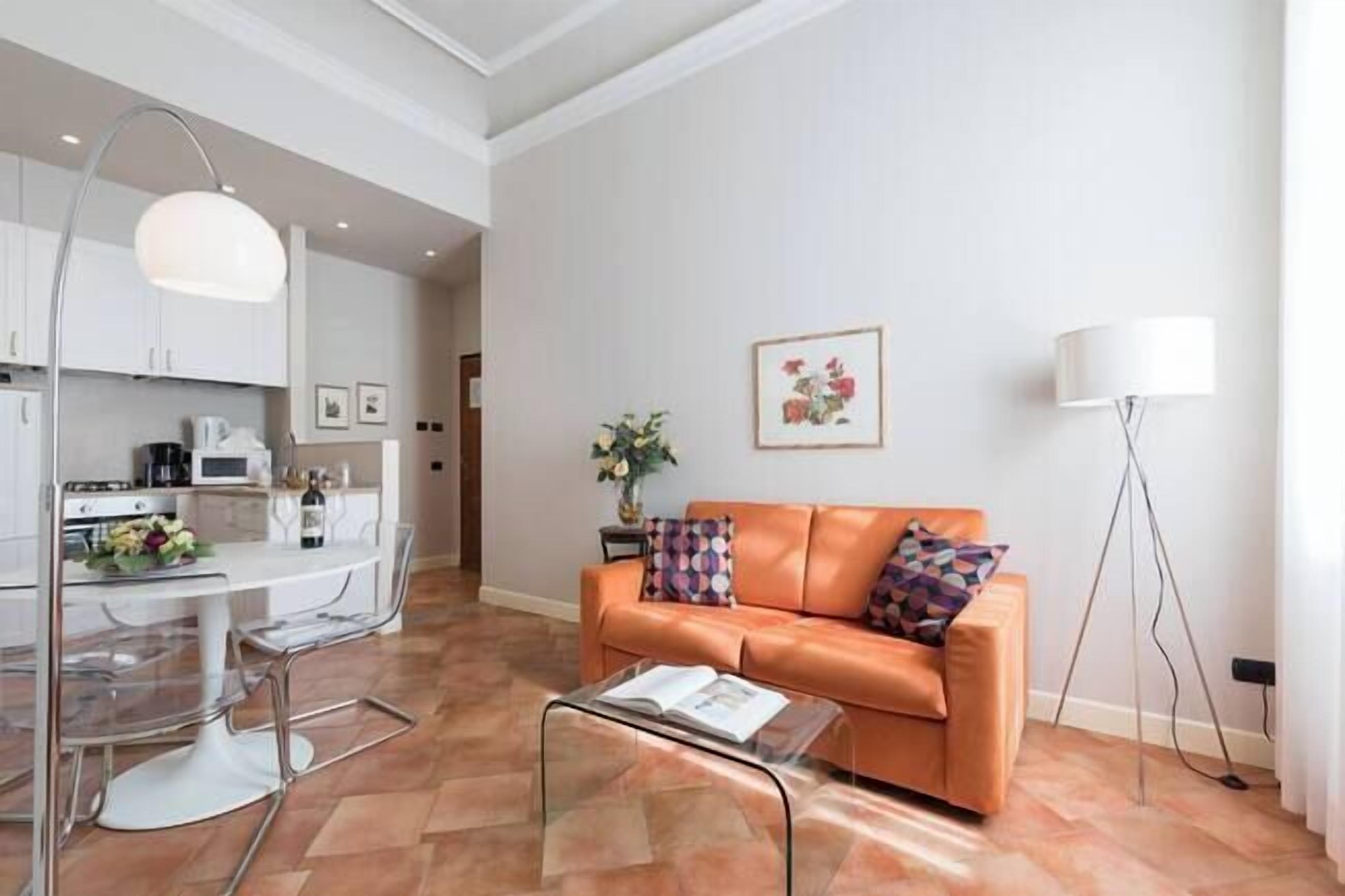 A modern living room with a glass coffee table, a leather sofa, and a dining area with a white table and chairs.