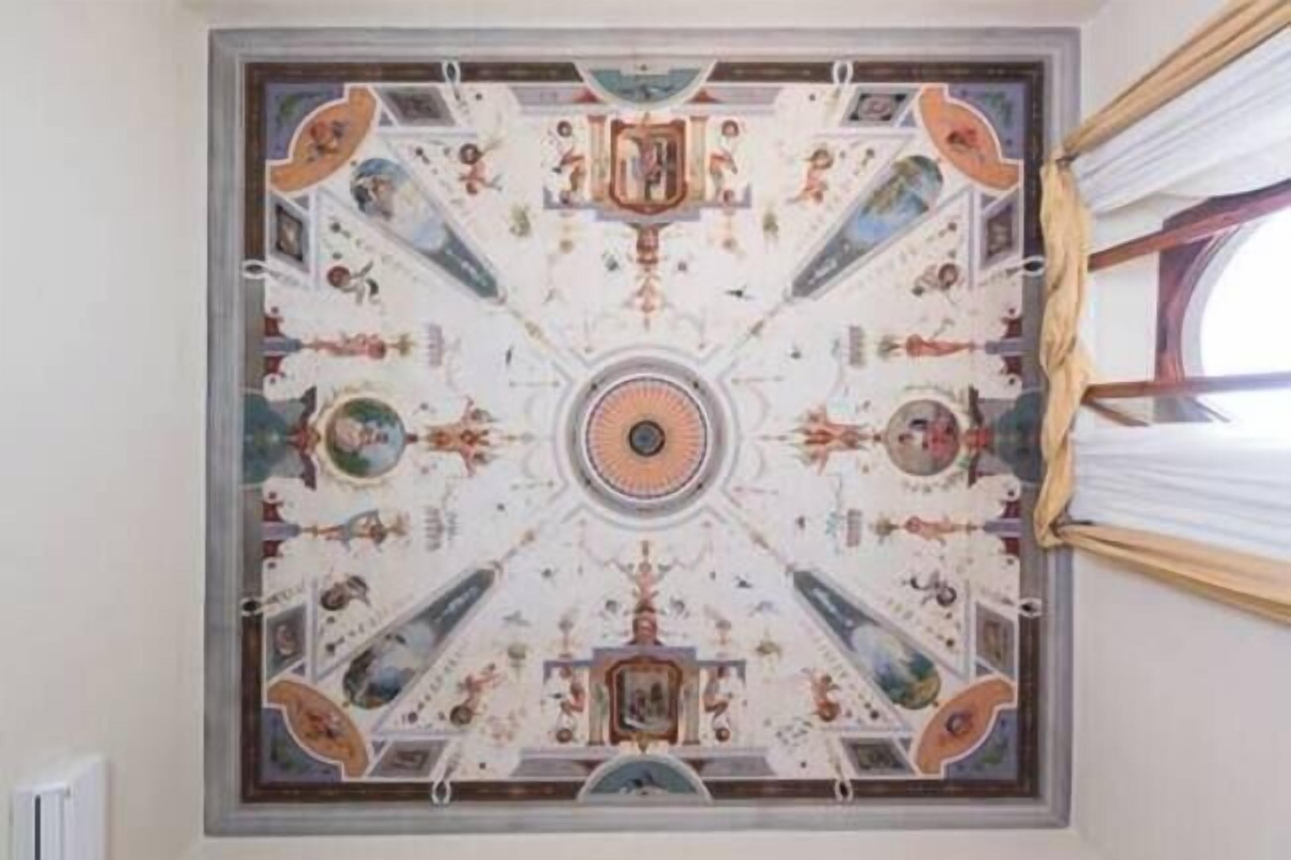 A ceiling with a symmetrical design featuring a central circular motif and surrounding panels with various figures and scenes.