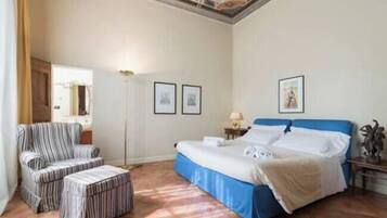 Una habitación de hotel con una cama, una silla, una mesita auxiliar y una lámpara de pie.
