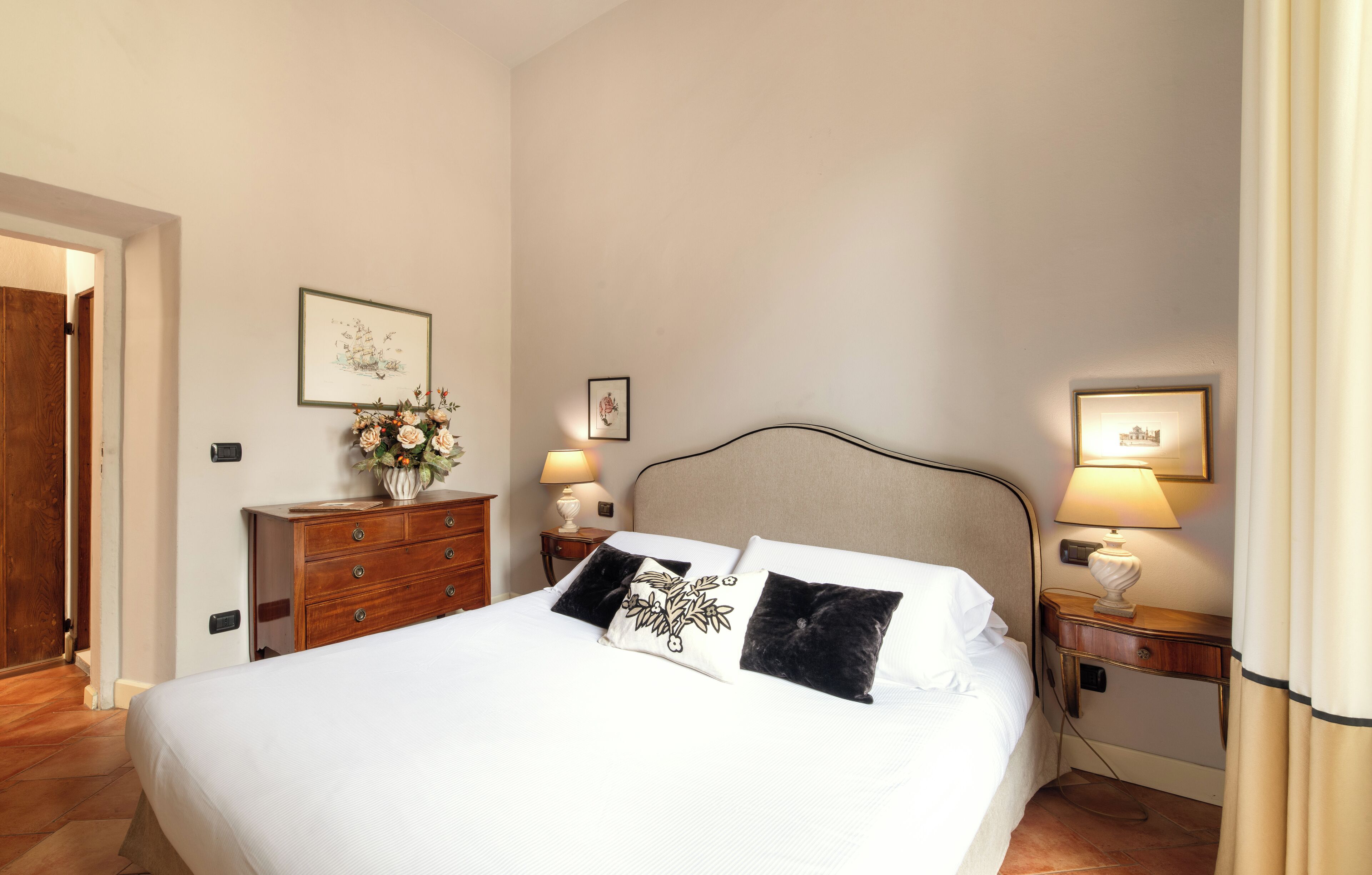 A neatly arranged bedroom with a large bed, two bedside tables with lamps, a wooden dresser, and framed artwork on the walls.